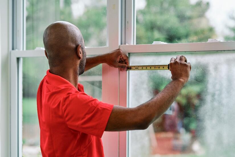 Man measuring double pane window with measuring tape